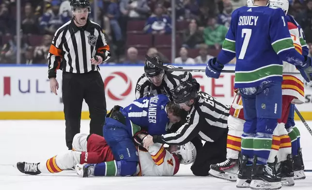 Linesmen Bevan Mills, back, and Tommy Hughes, right, try to separate Vancouver Canucks' Nils Hoglander (21) and Calgary Flames' Rasmus Andersson (4) as they get into scuffle after Andersson threw Hoglander to the ice during the third period of an NHL hockey game Tuesday, April 16, 2024, in Vancouver, British Columbia. (Darryl Dyck/The Canadian Press via AP)