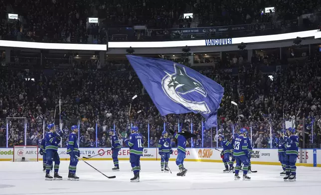 Vancouver Canucks players gather at center ice to raise their sticks to the fans after defeating the Calgary Flames in the team's home regular-season finale NHL hockey game Tuesday, April 16, 2024, in Vancouver, British Columbia. (Darryl Dyck/The Canadian Press via AP)