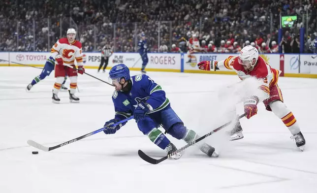 Vancouver Canucks' Conor Garland, left, turns away from Calgary Flames' MacKenzie Weegar while skating with the puck during the second period of an NHL hockey game Tuesday, April 16, 2024, in Vancouver, British Columbia. (Darryl Dyck/The Canadian Press via AP)