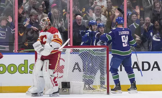Calgary Flames goalie Jacob Markstrom, left, stands in front of the net as Vancouver Canucks' Elias Pettersson, Nils Hoglander and Nikita Zadorov, from left, celebrate Hoglander's goal during the first period of an NHL hockey game Tuesday, April 16, 2024, in Vancouver, British Columbia. (Darryl Dyck/The Canadian Press via AP)