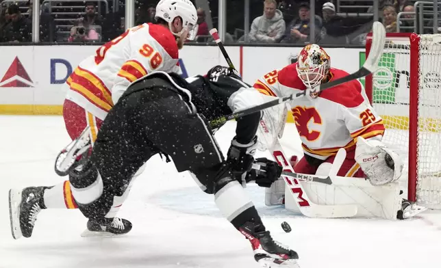 Los Angeles Kings defenseman Mikey Anderson, center, shoots the puck as Calgary Flames defenseman Ilya Solovyov, left, and goaltender Jacob Markstrom defend during the second period of an NHL hockey game Thursday, April 11, 2024, in Los Angeles. (AP Photo/Mark J. Terrill)