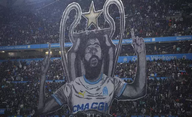 Marseille supporters raise a banner depicting humorist Redouane Bougheraba prior to the start of the French League One soccer match between Marseille and Paris at the Velodrome stadium in Marseille, south of France, Sunday, March 31, 2024. (AP Photo/Daniel Cole)