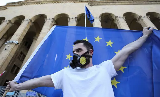 A demonstrator holds a EU flag as other gather outside the parliament building in Tbilisi, Georgia, on Wednesday, April 17, 2024, to protest against "the Russian law" similar to a law that Russia uses to stigmatize independent news media and organizations seen as being at odds with the Kremlin. (AP Photo/Zurab Tsertsvadze)
