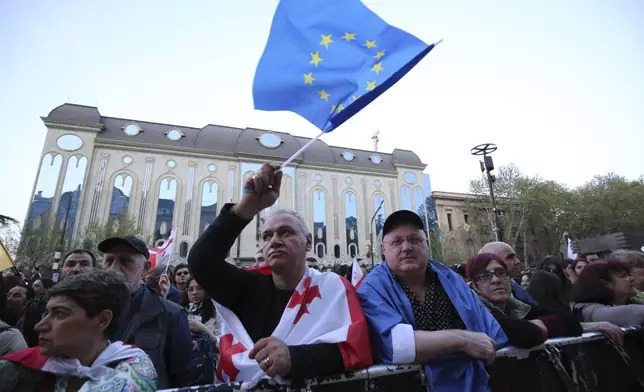 Demonstrators, one of them waves a EU flag, gather outside the parliament building in Tbilisi, Georgia, on Wednesday, April 17, 2024, to protest against "the Russian law" similar to a law that Russia uses to stigmatize independent news media and organizations seen as being at odds with the Kremlin. (AP Photo/Zurab Tsertsvadze)