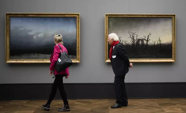 A couple walk in front of the painings 'Monk By The Sea', left, and ' Abby Among The Oaks' during a press preview of the exhibition 'Caspar David Friedrich. Infinite Landscapes' at the Alte Nationalgalerie museum in Berlin, Wednesday, April 17, 2024. The exhibition marking the 250th birthday of Caspar David Friedrich and will run from April 19 until August 4, 2024. (AP Photo/Markus Schreiber)