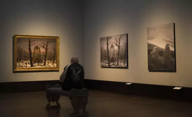 A man sits in front of a copy of Caspa David Friedrich's painting Monastery Cemetery In Snow' during a press preview of the exhibition 'Caspar David Friedrich. Infinite Landscapes' at the Alte Nationalgalerie museum in Berlin, Germany, Germany, Wednesday, April 17, 2024. A major show of Caspar David Friedrich's iconic landscapes that marks the 250th anniversary of his birth is opening in Berlin, the city where he made his breakthrough and where an exhibition in 1906 kicked off an an enduring revival in interest in the German Romantic master. (AP Photo/Markus Schreiber)