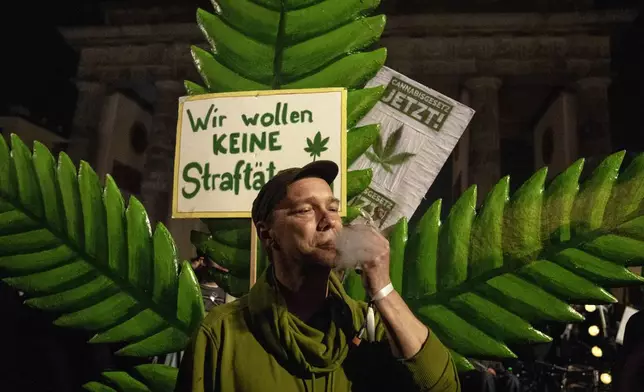 A man takes a puff from a marijuana cigarette in front of the Brandenburg Gate and a placard reading "We don't want to be offenders!" during the 'Smoke-In' event in Berlin, Germany, Monday, April 1, 2024. Starting 1 April, Germany has legalised cannabis for personal use. As per the new law, Adults aged 18 and over will be allowed to carry up to 25 grams of cannabis for their own consumption. (AP Photo/Ebrahim Noroozi)