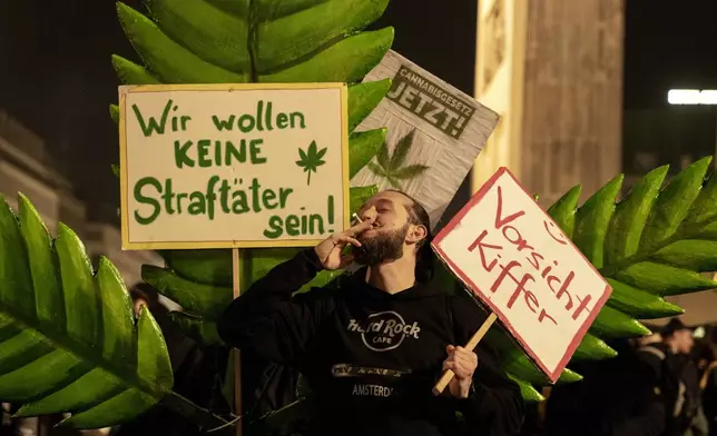 A man takes a puff from a marijuana cigarette next to a placard reading "We don't want to be offenders!" in front of the Brandenburg Gate during the "Smoke-In" event in Berlin, Germany, Monday, April 1, 2024. Starting 1 April, Germany has legalised cannabis for personal use. As per the new law, Adults aged 18 and over will be allowed to carry up to 25 grams of cannabis for their own consumption. (AP Photo/Ebrahim Noroozi)