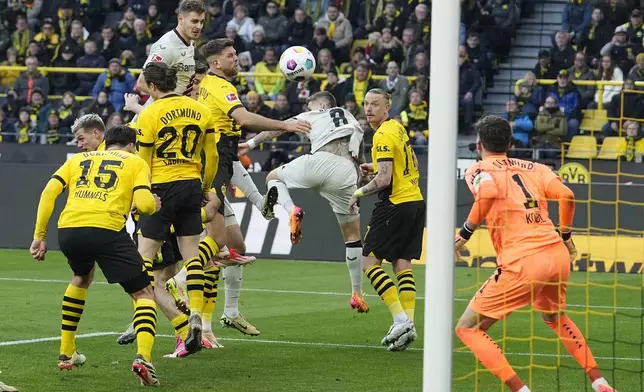 Leverkusen's Josip Stanisic, up, scores for his team in the last minute during the German Bundesliga soccer match between Borussia Dortmund and Bayer Leverkusen in Dortmund, Germany, Sunday, April 21, 2024. The match ended 1-1, Leverkusen is unbeaten since 45 matches. (AP Photo/Martin Meissner)