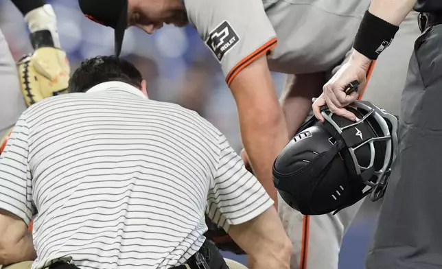 A San Francisco Giants trainer checks the leg of pitcher Keaton Winn after he was hit by ground ball during the sixth inning of a baseball game against the Miami Marlins, Wednesday, April 17, 2024, in Miami. (AP Photo/Marta Lavandier)