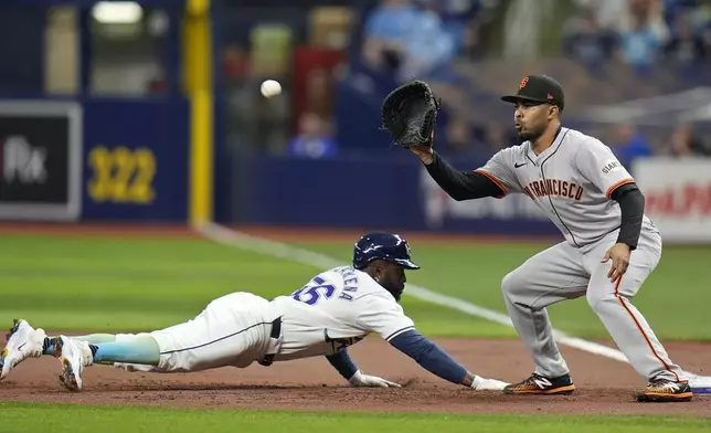 Tampa Bay Rays' Randy Arozarena, left, dives back to first ahead of the pickoff throw to San Francisco Giants first baseman LaMonte Wade Jr. during the first inning of a baseball game Friday, April 12, 2024, in St. Petersburg, Fla. (AP Photo/Chris O'Meara)
