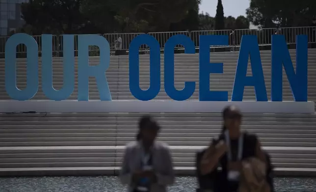 People walk in front of an 'Our Ocean' sign during the 'Our Ocean Conference' at the Stavros Niarchos Foundation Cultural Center in Athens, Greece, Tuesday, April 16, 2024. Greece aims to create two large marine parks as part of a 780 million euro ($830 million) program to protect biodiversity and marine ecosystems, with the plans to be formally announced at an international oceans conference starting in Athens Tuesday. (AP Photo/Michael Varaklas)