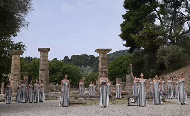 Actress Mary Mina, playing high priestess, right, holds a torch with the flame during the official ceremony of the flame lighting for the Paris Olympics, at the Ancient Olympia site, Greece, Tuesday, April 16, 2024. The flame will be carried through Greece for 11 days before being handed over to Paris organizers on April 26. (AP Photo/Thanassis Stavrakis)