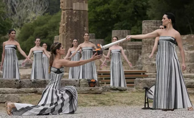 Actress Mary Mina, playing high priestess, right, lights a torch during the official ceremony of the flame lighting for the Paris Olympics, at the Ancient Olympia site, Greece, Tuesday, April 16, 2024. The flame will be carried through Greece for 11 days before being handed over to Paris organizers on April 26. (AP Photo/Thanassis Stavrakis)