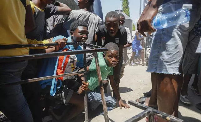 FILE - Youth take cover after hearing gunshots at a public school that serves as a shelter for people displaced by gang violence, in Port-au-Prince, Haiti, March 22, 2024. (AP Photo/Odelyn Joseph, File)