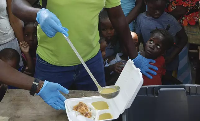 FILE - A server ladles soup into a container as children line up to receive food at a shelter for families displaced by gang violence, in Port-au-Prince, Haiti, March 14, 2024. (AP Photo/Odelyn Joseph, File)