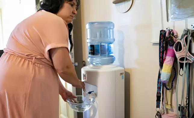 Richelle Dietz fills up a bowl of water from the water dispensary at her home, Monday, April 22, 2024, in Honolulu, Hawaii. The Dietz family relies on bi-weekly water deliveries for basic needs since their water was tainted in 2021. (AP Photo/Mengshin Lin)