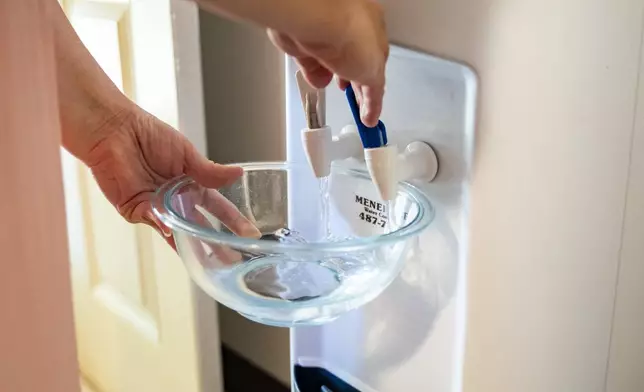Richelle Dietz fills up a bowl of water from the water dispensary at her home on Monday, April 22, 2024, in Honolulu, Hawaii. The Dietz family relies on bi-weekly water deliveries for basic needs since their water was tainted in 2021. (AP Photo/Mengshin Lin)