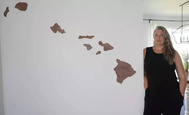 Amy Chadwick, stands by map of Hawaii at her current home Monday, April 8, 2024, in Satellite Beach, Fla. Chadwick, a victim of the fires in Hawaii moved to Florida where she could stretch her homeowners insurance dollars while she waits for her lot to be cleared and for permission to rebuild. (AP Photo/John Raoux)