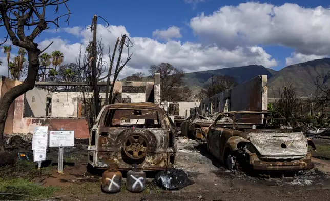 FILE - Burned cars and propane tanks with markings on them sit outside a house destroyed by wildfire, Friday, Dec. 8, 2023, in Lahaina, Hawaii. An acute housing shortage hitting fire survivors on the Hawaiian island of Maui is squeezing out residents even as they try to overcome the loss of loved ones, their homes and their community. (AP Photo/Lindsey Wasson, File)