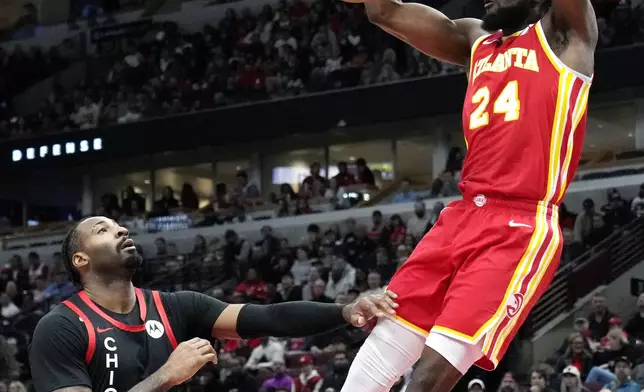 Atlanta Hawks forward Bruno Fernando, right, hangs from the rim after dunking against Chicago Bulls center Andre Drummond during the first half of an NBA basketball game in Chicago, Monday, April 1, 2024. (AP Photo/Nam Y. Huh)