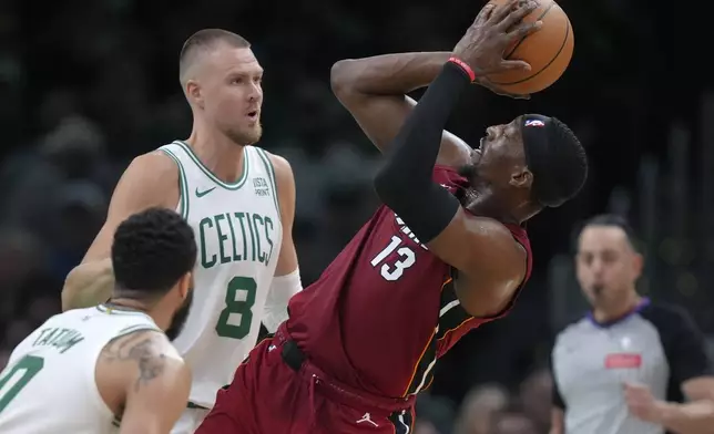 Miami Heat center Bam Adebayo (13) looks to shoot at the basket as Boston Celtics center Kristaps Porzingis (8) and forward Jayson Tatum (0) defend in the first half of Game 1 of an NBA basketball first-round playoff series, Sunday, April 21, 2024, in Boston. (AP Photo/Steven Senne)