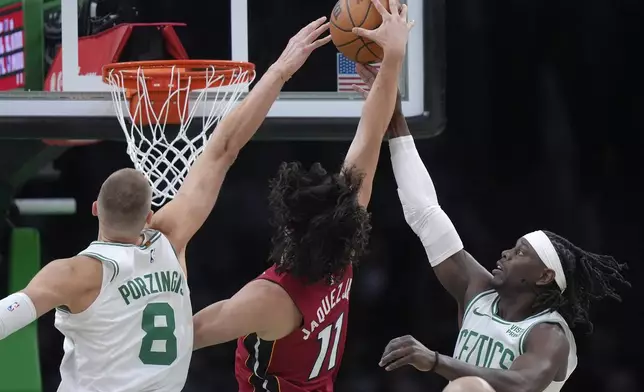 Miami Heat guard Jaime Jaquez Jr. (11) shoots at the basket as Boston Celtics center Kristaps Porzingis (8) and guard Jrue Holiday, right, defend in the first half of Game 1 of an NBA basketball first-round playoff series, Sunday, April 21, 2024, in Boston. (AP Photo/Steven Senne)
