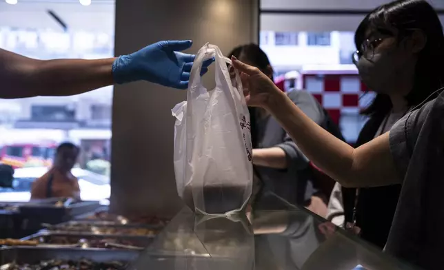 A customer collects a takeaway food plastic bag at Kuen Fat Kitchen in Hong Kong, Wednesday, April 10, 2024. Hong Kong has long been a major producer and consumer of great food, and a great amount of plastic and Styrofoam to go with it. That’s going to change as new legislation aiming to stop the sale and distribution of Styrofoam products and single-use plastic cutlery went into effect on Monday, April 22, 2024. (AP Photo/Louise Delmotte)