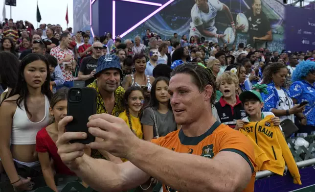 Australia's Michael Hooper takes a selfie with fans at the end of the men's third place match between Australia and Ireland in the Hong Kong Sevens rugby tournament in Hong Kong, Sunday, April 7, 2024. (AP Photo/Louise Delmotte)