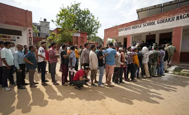 A man squats to rest as people queue up to vote during the second round of voting in the six-week-long national election in Jammu, India, Friday, April 26, 2024. (AP Photo/Channi Anand)