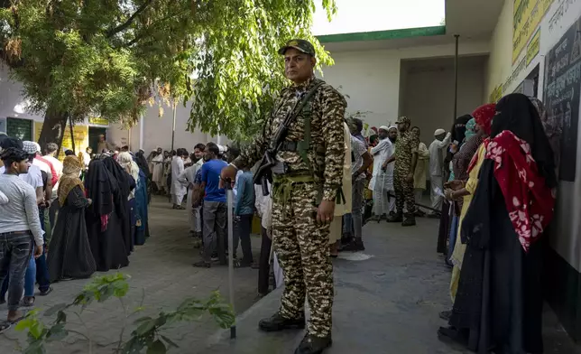 A security personnel stands guard as people queue up to vote during the second round of voting in the six-week-long national election in Nahal village near Meerut, in Uttar Pradesh, India, Friday, April 26, 2024. (AP Photo/Altaf Qadri)