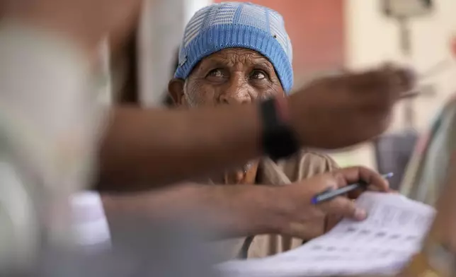 An elderly voter waits to cast his vote as an election official checks for his name in the voters list during the second round of voting in the six-week-long national election in Jammu, India, Friday, April 26, 2024. (AP Photo/Channi Anand)