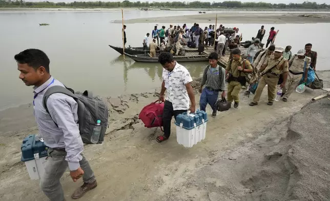 Polling officials and security personnels carry Electronic Voting Machines (EVMs) and other election material off a boat after crossing the Brahmaputra river on the eve of the national election at Baghmora Chapori (small island) of Majuli, about 350km (218 miles) east of the state capital Guwahati, India, Thursday, April 18, 2024. (AP Photo/Anupam Nath)