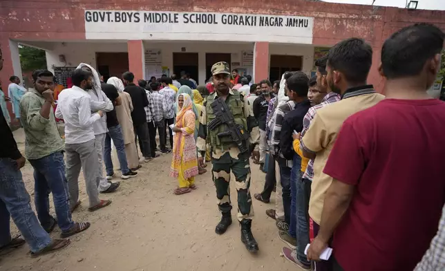 A paramilitary soldier stands guard as people queue up to vote during the second round of voting in the six-week-long national election in Jammu, India, Friday, April 26, 2024. (AP Photo/Channi Anand)
