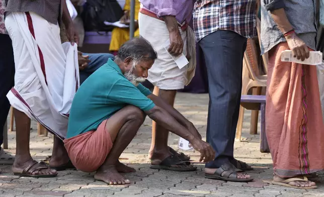 A man squats to rest as people queue up to vote during the second round of voting in the six-week-long national election near Palakkad, in Indian southern state of Kerala, Friday, April 26, 2024. (AP Photo/Manish Swarup)