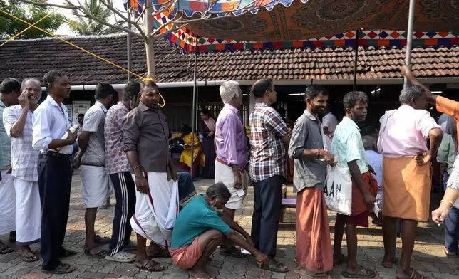 A man squats to rest as he waits with others in a queue to vote during the second round of voting in the six-week-long national election near Palakkad, in Indian southern state of Kerala, Friday, April 26, 2024. (AP Photo/Manish Swarup)