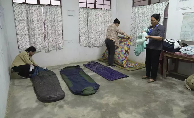 Polling officers, left to right, Neke W Konyak, 29, Dekule Kapfo, 34, and Nukutholu Nienu, 44, make their beds on a concrete floor, on the eve of polling in Chedema village, in the northeastern Indian state of Nagaland, Thursday, April 18, 2024. (AP Photo/Yirmiyan Arthur)