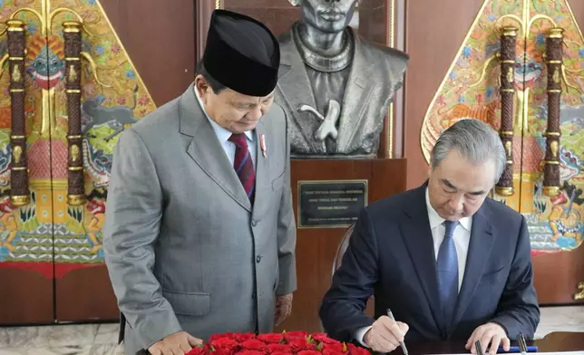 Indonesian President-elect and current Defense Minister Prabowo Subianto, left, stands next to Chinese Foreign Minister Wang Yi as Wang signs a guest book in Jakarta, Indonesia, Thursday, April 18, 2024. (AP Photo/Achmad Ibrahim/Pool)