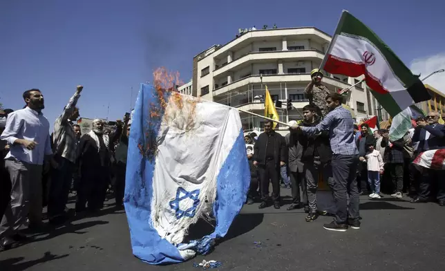 Iranian demonstrators burn a representation of the Israeli flag as one of them waves their country's flag during an annual rally to mark Quds Day, or Jerusalem Day, to support the Palestinians in Tehran, Iran, Friday, April 5, 2024. In the rally in Tehran, thousands attended a funeral procession for the seven Revolutionary Guard members killed in an airstrike widely attributed to Israel that destroyed Iran's Consulate in the Syrian capital on Monday. (AP Photo/Vahid Salemi)