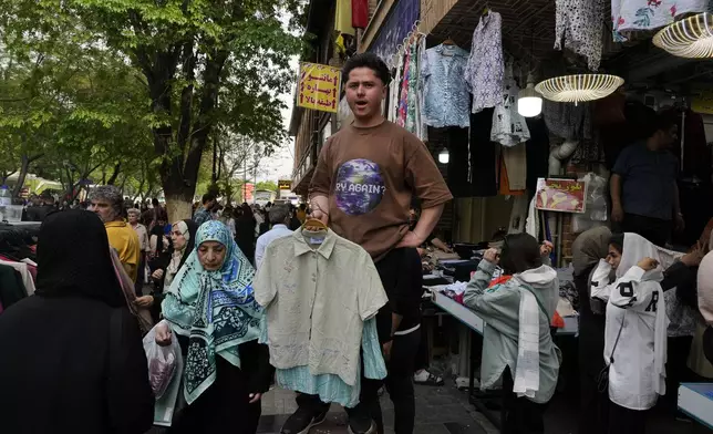 A shopkeeper advertises women's clothes of a shop at the old main bazaar in Tehran, Iran, Tuesday, April 16, 2024. Israel says it is poised to retaliate against Iran, risking further expanding the shadow war between the two foes into a direct conflict after an Iranian attack over the weekend sent hundreds of munitions into Israeli airspace. (AP Photo/Vahid Salemi)