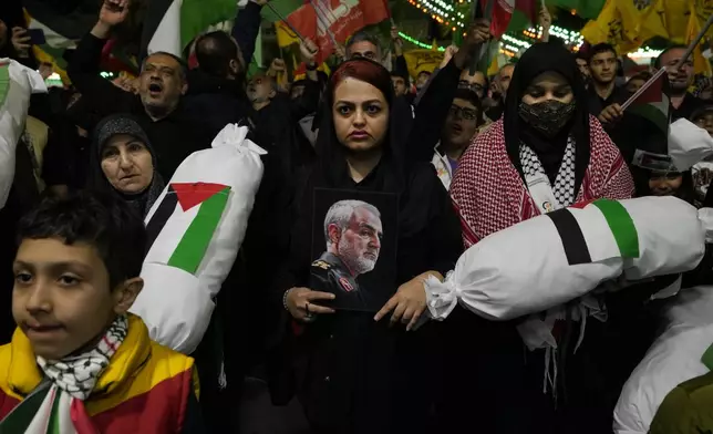 An Iranian protester holds a poster of the late Iranian Revolutionary Guard Gen. Qassem Soleimani, who was killed in a U.S. drone attack in 2020, as two others hold the symbolic mock bodies of the Palestinian children during their anti-Israeli gathering to condemn killing members of the Iranian Revolutionary Guard in Syria, at the Felestin (Palestine) Sq. in downtown Tehran, Iran, Monday, April 1, 2024. An Israeli airstrike that demolished Iran's consulate in Syria killed two Iranian generals and five officers, Syrian and Iranian officials said Monday. (AP Photo/Vahid Salemi)