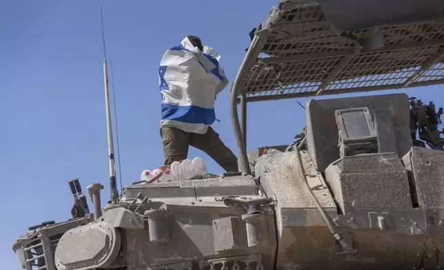 An Israeli soldier holds a country's flag on top of an armoured personnel carriers (APC) near Israel's border with Gaza, in southern Israel, Monday, April 15, 2024. (AP Photo/Ohad Zwigenberg)