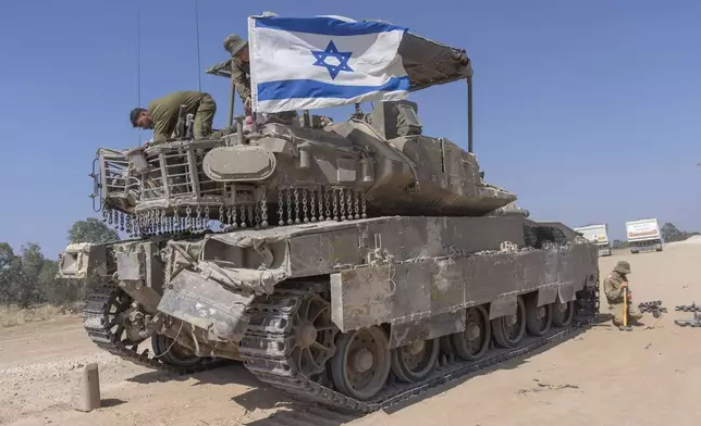 An Israeli soldier attaches an Israeli flag on top of an armoured personnel carriers (APC) near Israel's border with Gaza, in southern Israel, Monday, April 15, 2024. (AP Photo/Ohad Zwigenberg)