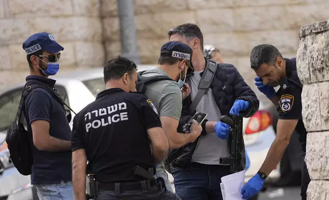 Israeli police examine a submachine gun recovered near the scene of a suspected ramming attack that wounded three people on the eve of the Jewish holiday of Passover, in Jerusalem, Monday, April 22, 2024. Israeli police say a car slammed into pedestrians in Jerusalem on Monday, wounding three people lightly in an apparent attack.(AP Photo/Ohad Zwigenberg)