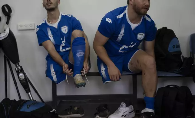 Israel Amputee Football Team players Shaked Bitton left, and Ben Binyamin wear their soccer cleats before a practice session in Ramat Gan, Thursday, April 11, 2024. The team practices two evenings a week at the stadium in the Tel Aviv suburb of Ramat Gan, first with warm-ups and drills, then practice games - each man undeterred by the absence of an arm or a leg from an accident, a war injury or a birth defect. (AP Photo/Leo Correa)