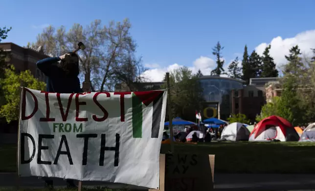 A student at the University of Oregon sets up a sign that reads "Divest from death" as students set up a tent encampment at the university to protest the Israel-Hamas war on Monday, April 29, 2024, in Eugene, Ore. (AP Photo/Jenny Kane)
