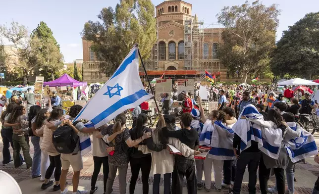 A group of pro-Israel supporters hold arms as they sing and dance outside a pro-Palestinian encampment on the UCLA campus Friday, April 26, 2024, in Los Angeles. As the death toll mounts in the war in Gaza and the humanitarian crisis worsens, protesters at universities across the country are demanding schools cut financial ties to Israel and divest from companies they say are enabling the conflict. (AP Photo/Damian Dovarganes)
