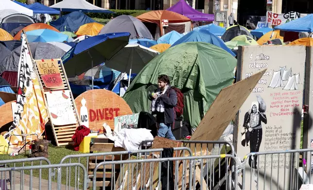 A man passes in front of the pro-Palestinian protesters' tents as they continued to occupy the grounds at University of California, Los Angeles, in front of Royce Hall, Monday, April 29, 2024, in Los Angeles. Security has surrounded the encampment after a skirmish broke out Sunday between pro-Palestinian protesters and Israel supporters. (David Crane/The Orange County Register via AP)