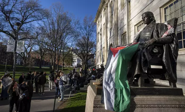 Students protesting against the war in Gaza, and passersby walking through Harvard Yard, are seen next to the statue of John Harvard, the first major benefactor of Harvard College, draped in the Palestinian flag, at an encampment at Harvard University in Cambridge, Mass., on Thursday, April 25, 2024. (AP Photo/Ben Curtis)