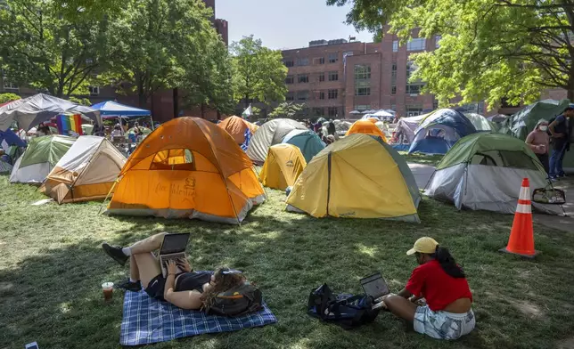 People sit in the shade near tents at an encampment by students protesting against the Israel-Hamas war at George Washington University on Monday, April 29, 2024, in Washington. (AP Photo/Mark Schiefelbein)